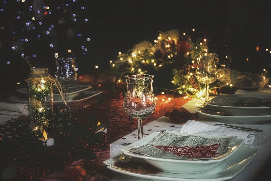 An image of a table set with plates, glasses and cutlery and Christmas lights as decoration.