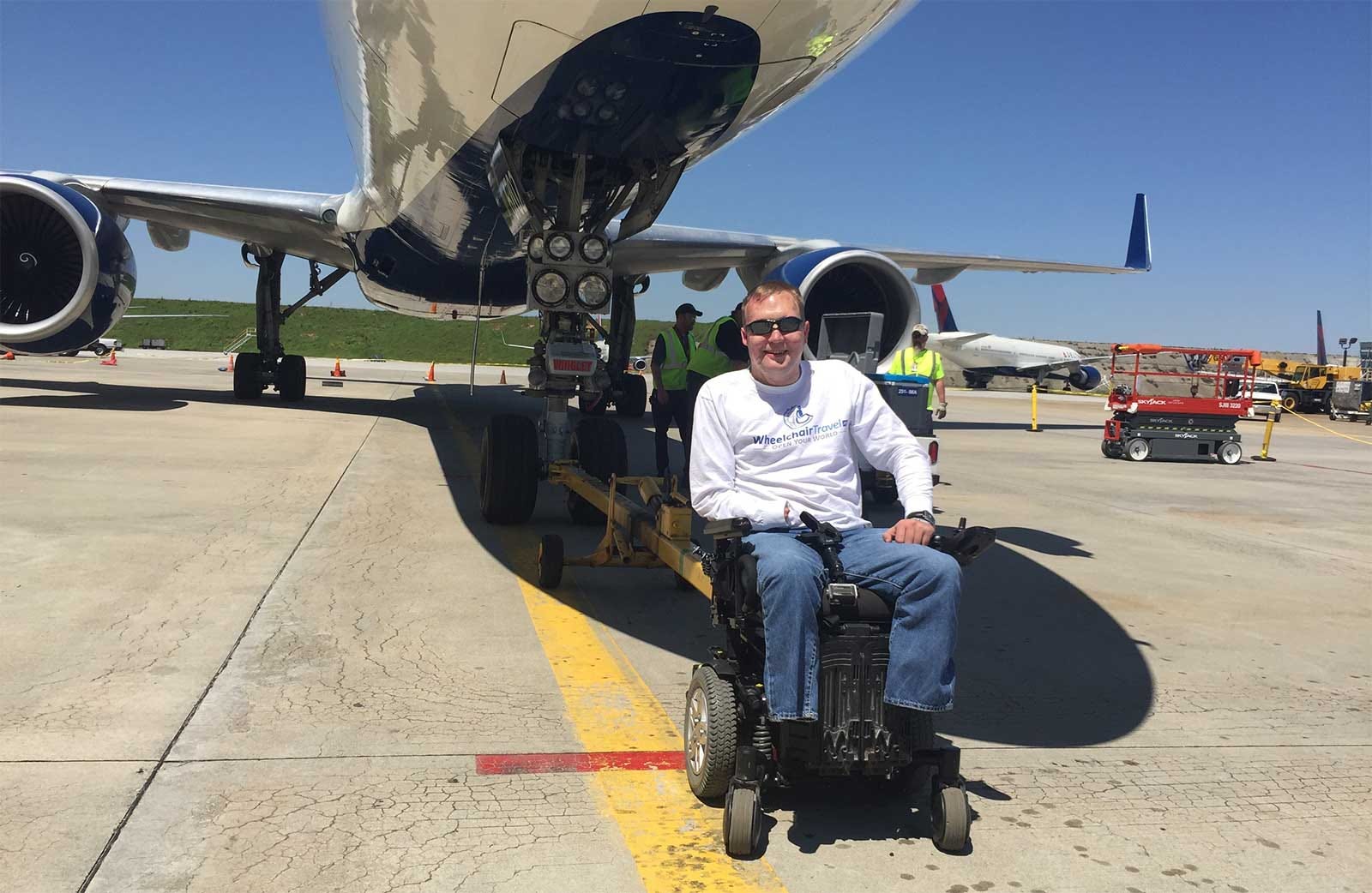 John seated in his wheelchair next to the front wheel of a Delta Air Lines Boeing 757 aircraft.