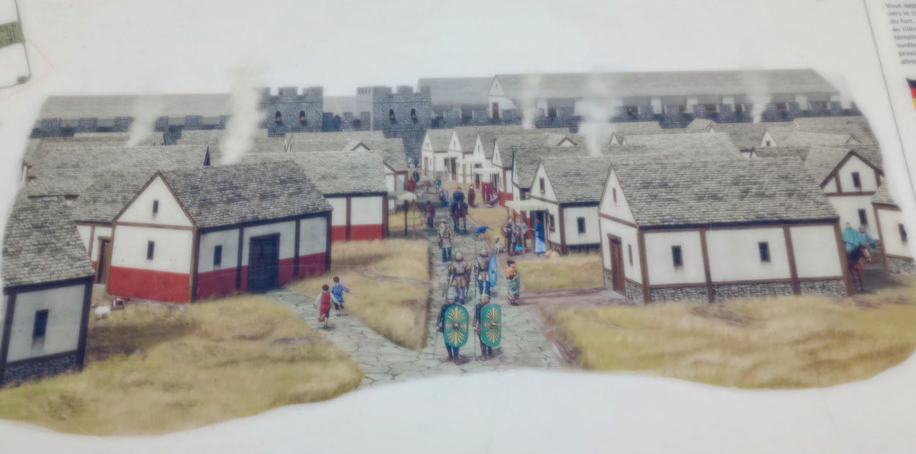 Village of one-story cottages, loosely strung along paved road, with Fort in background, smoke coming from chimneys, soldiers and civilians on street, including children running