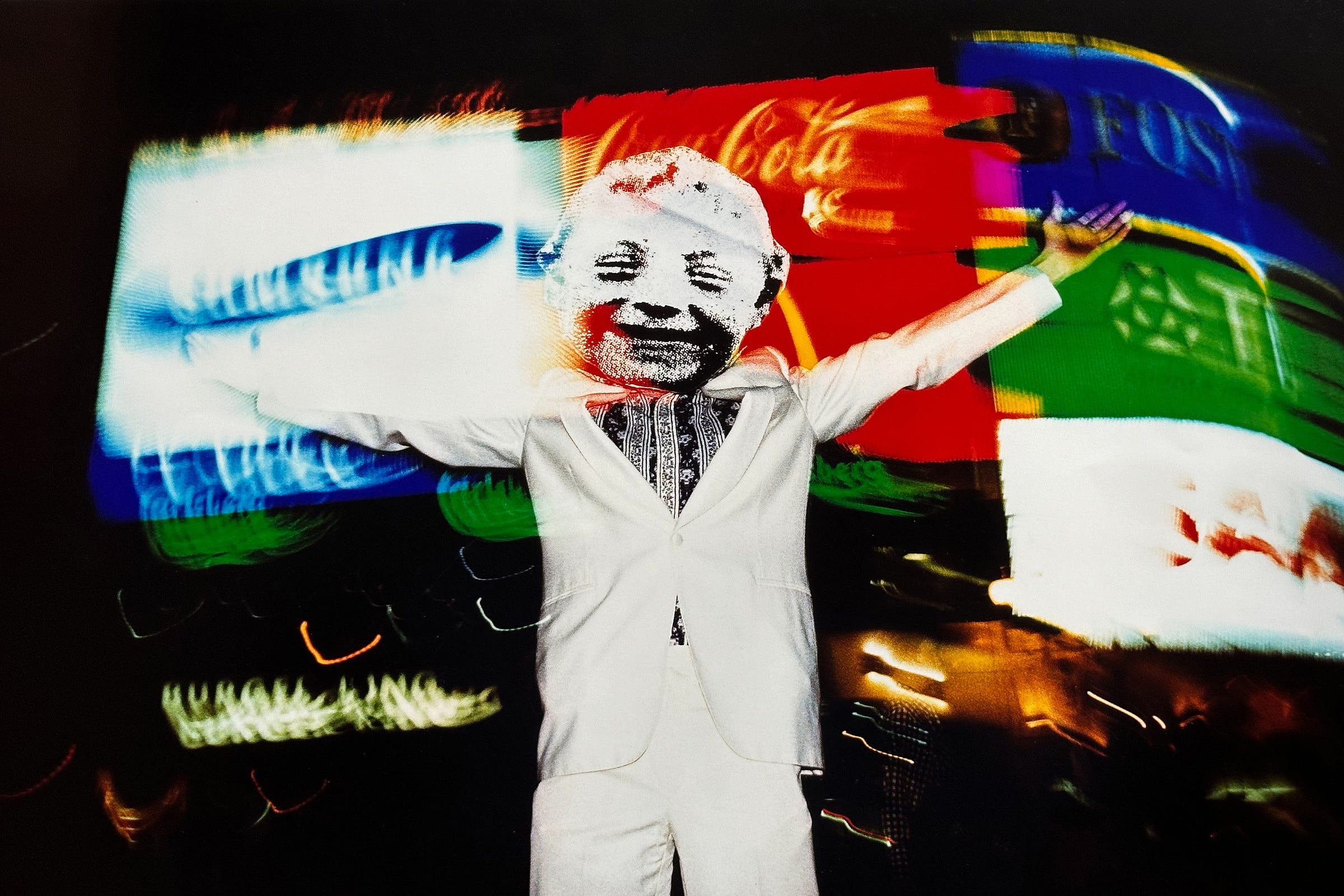 Man in a white suit wearing a cardboard mask with a blurry background of Piccadilly Circus, London