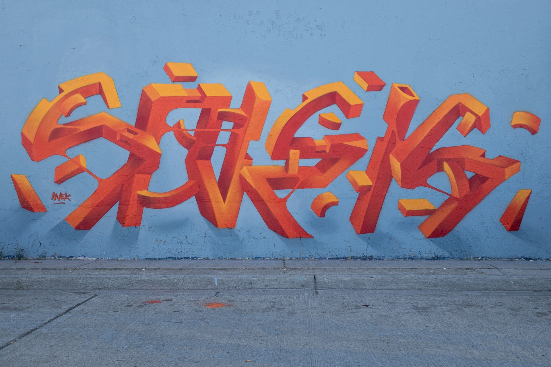 Un’opera di street art in Messico, firmata da Inek. Su uno sfondo celeste si staglia l’illustrazione di forme rosse in 3D che assomigliano a delle lettere astratte.