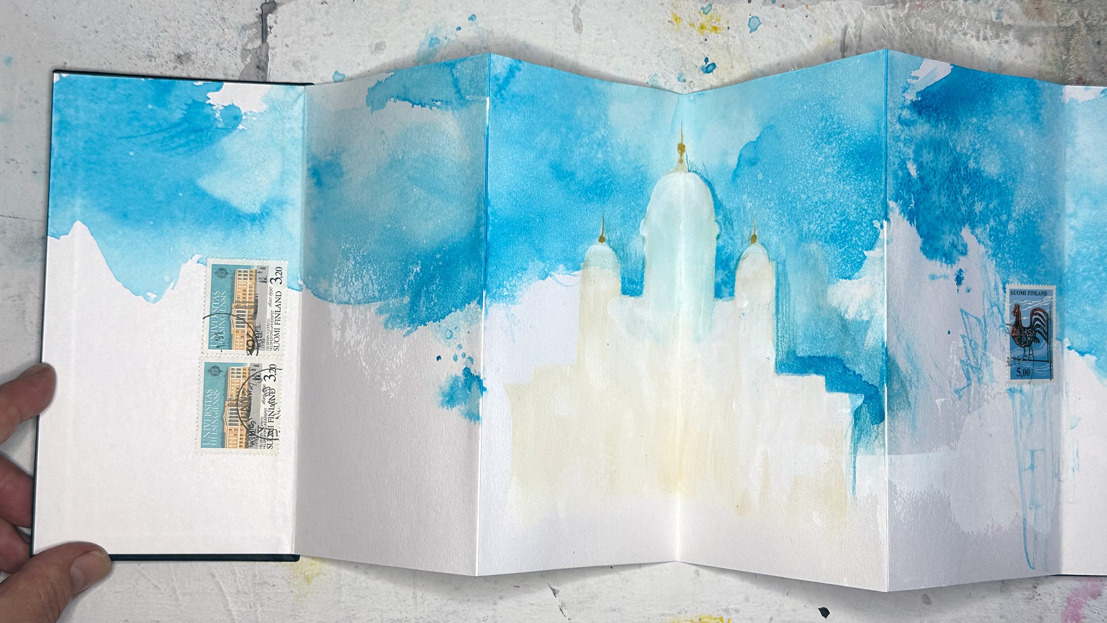 Pages in a concertina sketchbook showing blue ink wash in the 'sky' and a pale silhouette of a cathedral