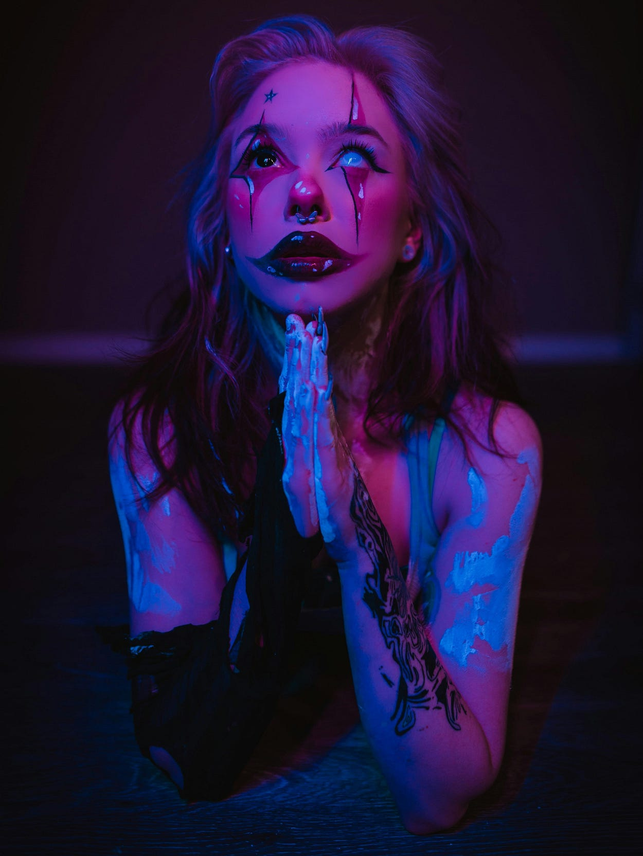 A woman with clown-like face paint poses with her hands pressed together in a prayer position. A woman with clown-like face paint poses with her hands pressed together in a prayer position.