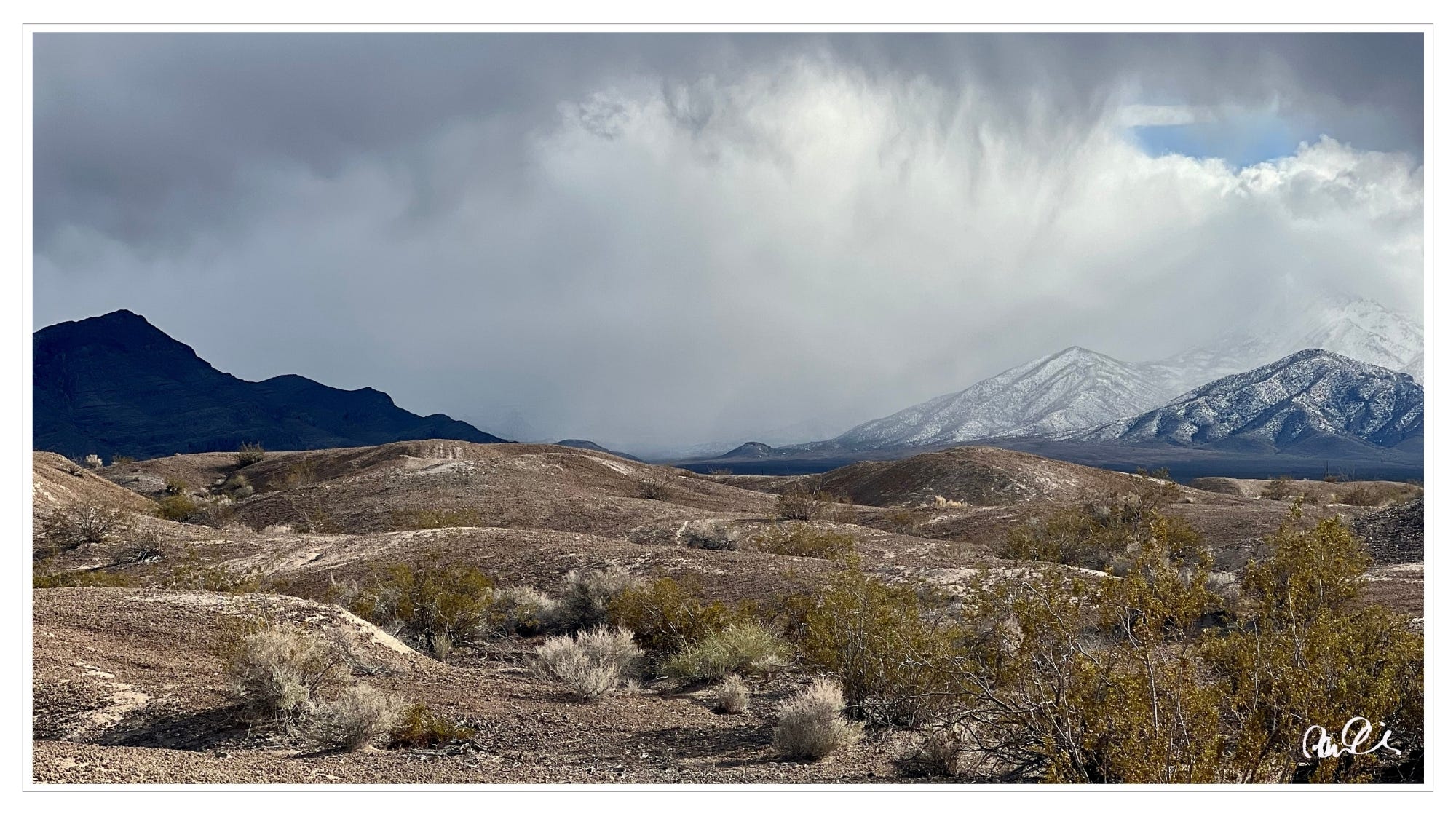 Snow-covered mountain ranges, dark clouds, Mohave Desert, NV