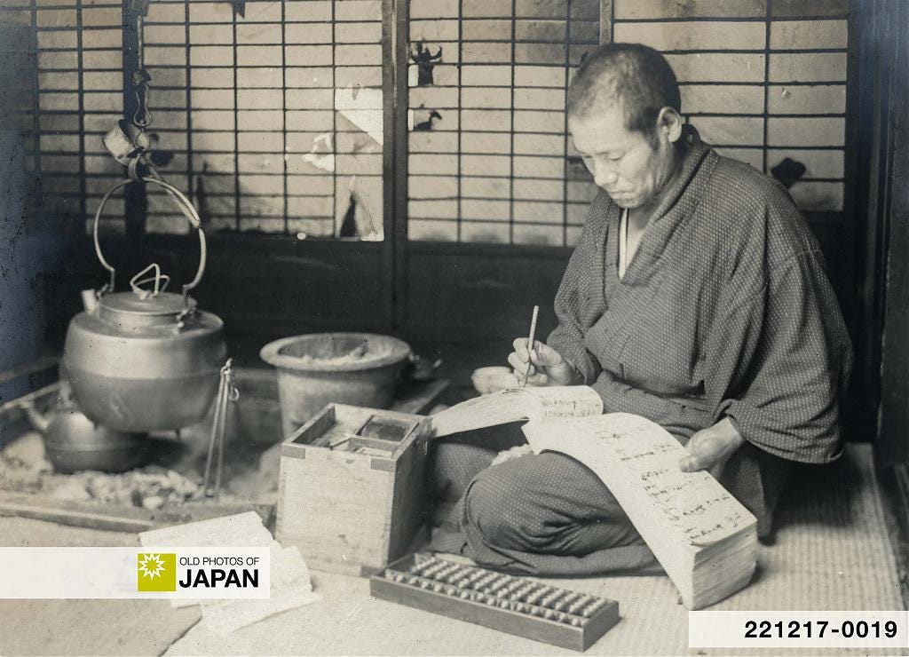 A Japanese businessman balancing the books next to the irori, 1910s