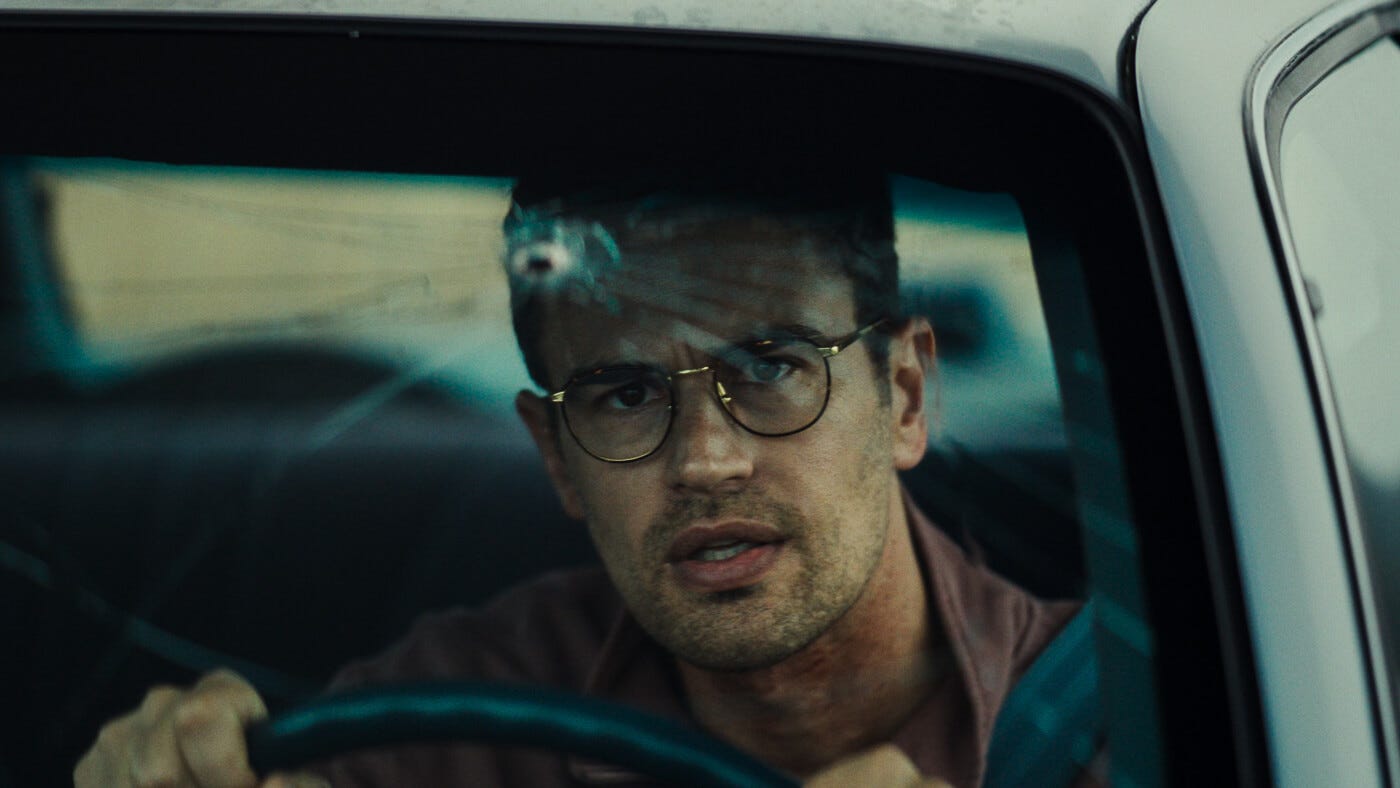 Theo James stares grimly ahead from behind the wheel, framed by a cracked windshield and reflected melancholy.