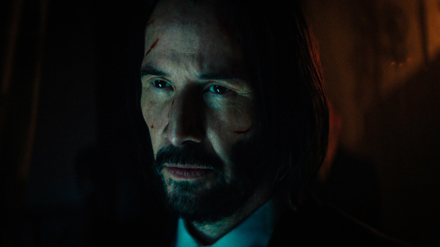 Close-up of John Wick, face bloodied and half-lit by opposing teal and amber light, looking forward with grim determination. Close-up of John Wick, face bloodied and half-lit by opposing teal and amber light, looking forward with grim determination.