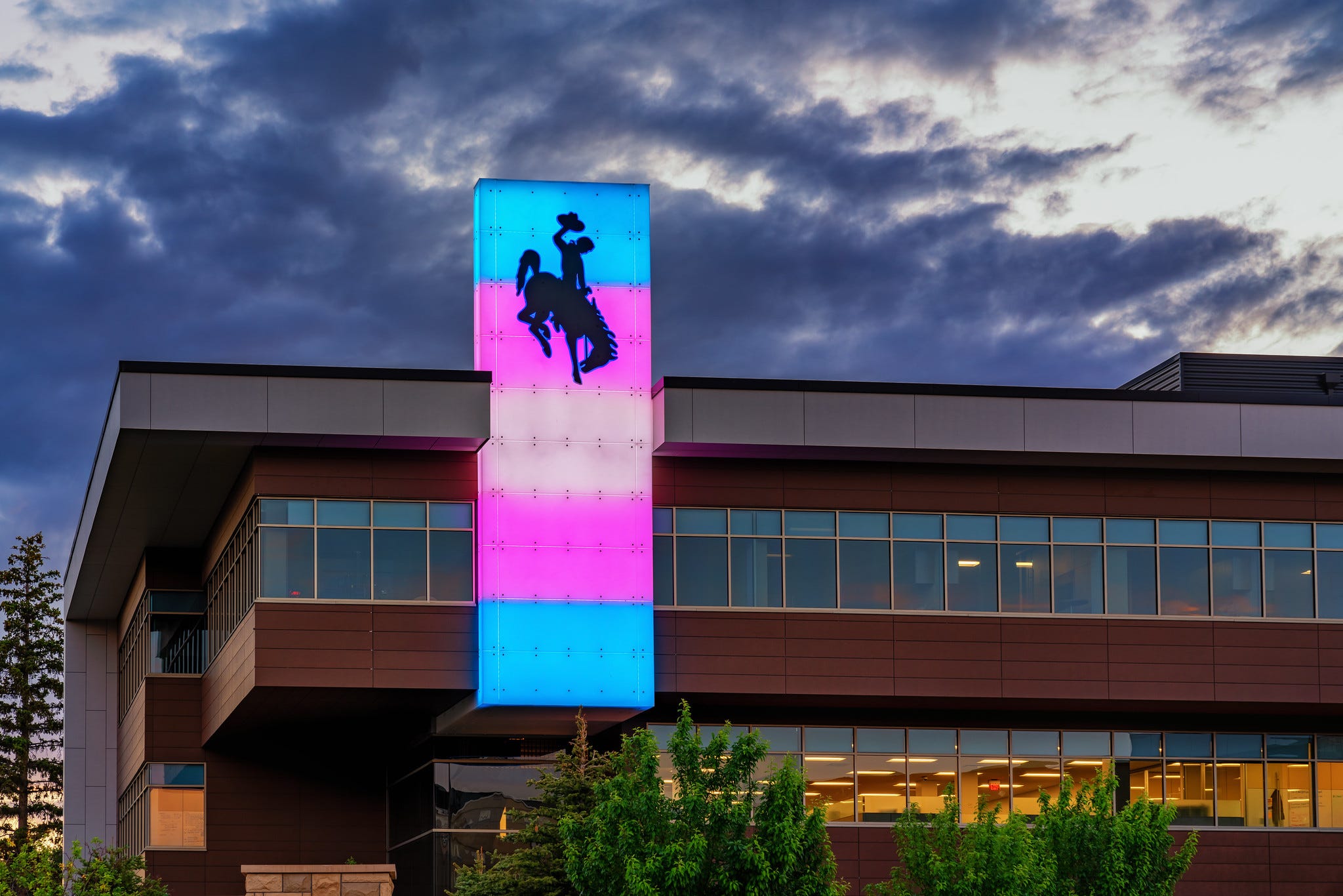 Blue pink and white lights illuminate a steamboat-adorned column on the Rochelle Center. HDR image showing dark cloudy skies in the background.