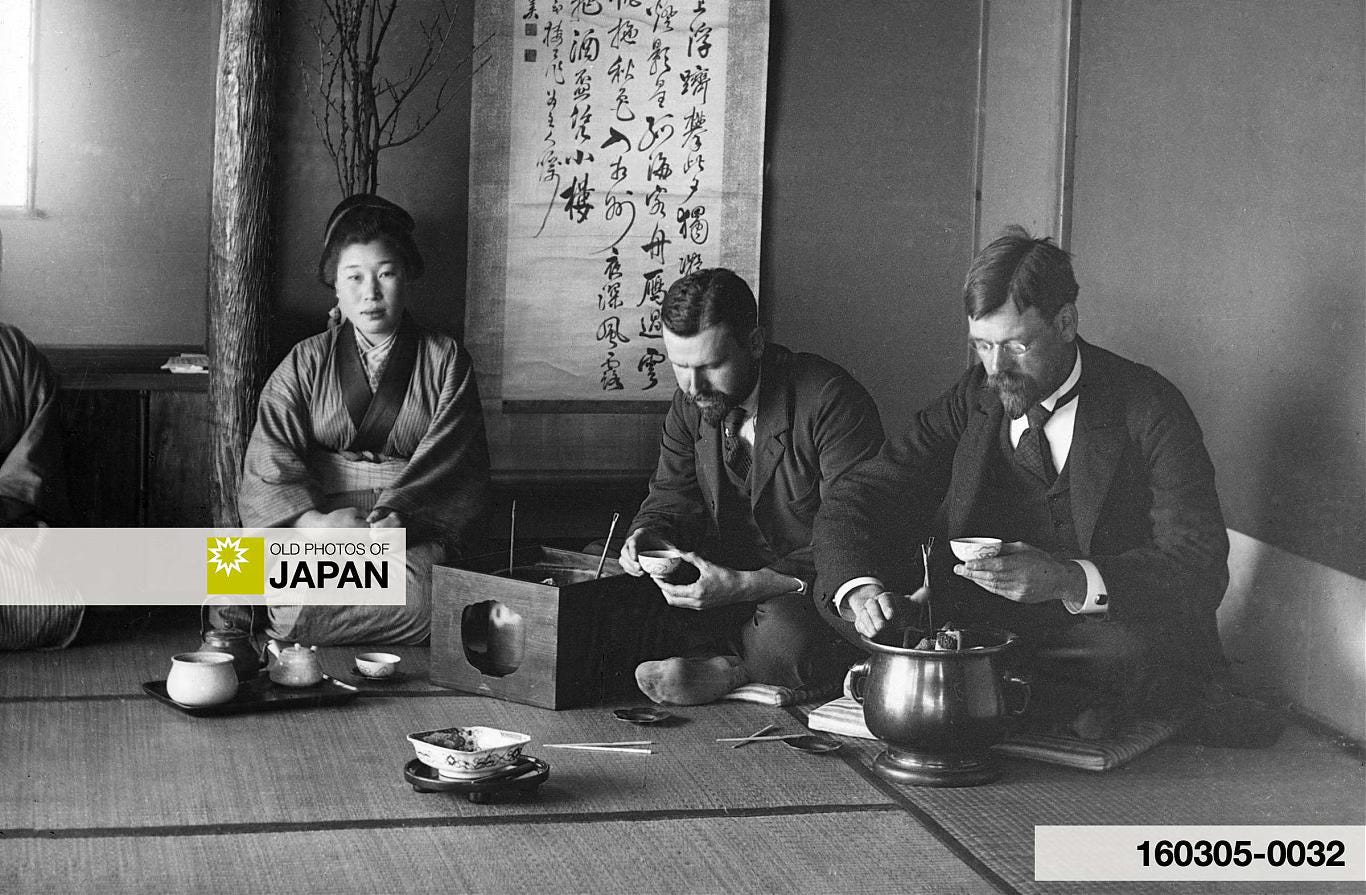 Two Western men are drinking Japanese tea while sitting close to hibachi, 1890s