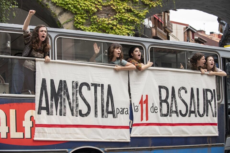 Una scena del film Las buenas compañías: cinque ragazze del collettivo femminista e amiche di Bea si affacciano dal finestrino dell’autobus sulla cui fiancata hanno appeso il manifesto “Amnistia para las 11 de Basauri”. Hanno i pugni alzati e un’espressione agguerrita mentre gridano i loro slogan.