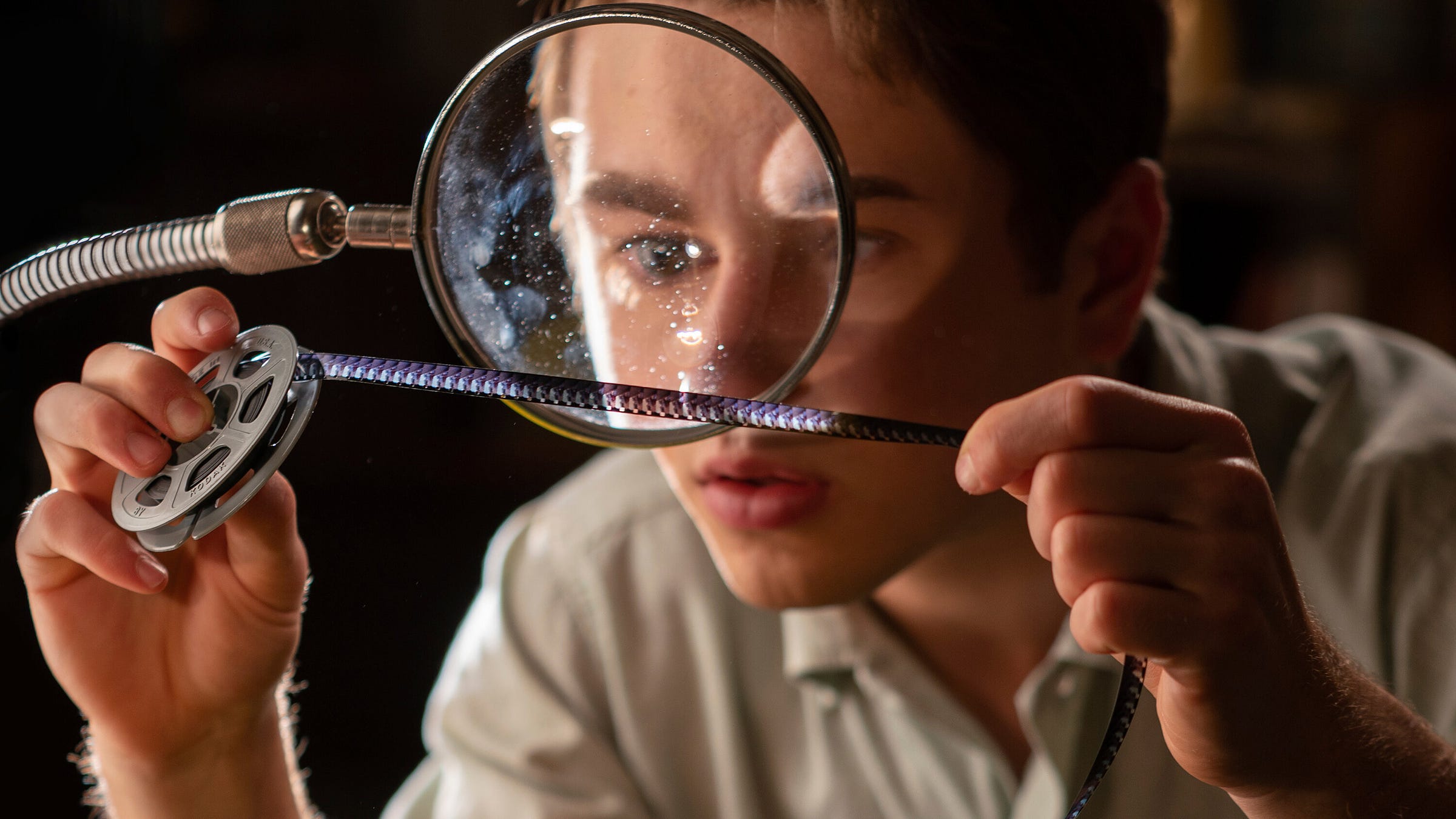 Gabriel Labelle as Samuel Fabelman looks at a reel of film through a magnifying glass.