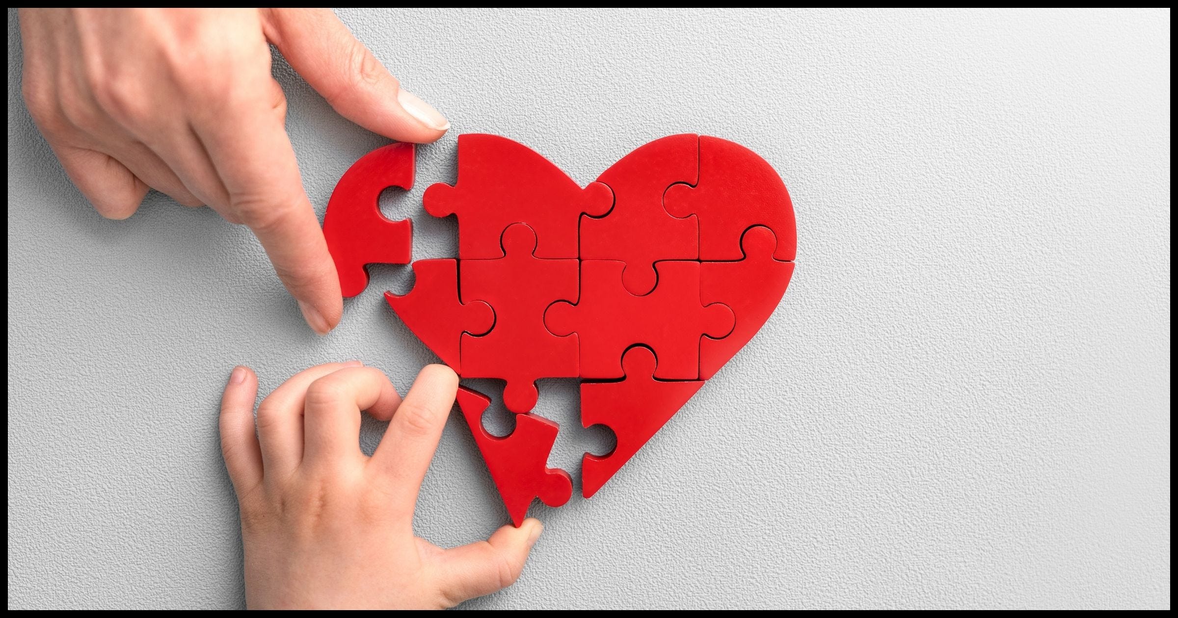Two hands putting peices into a jigsaw puzzle heart.