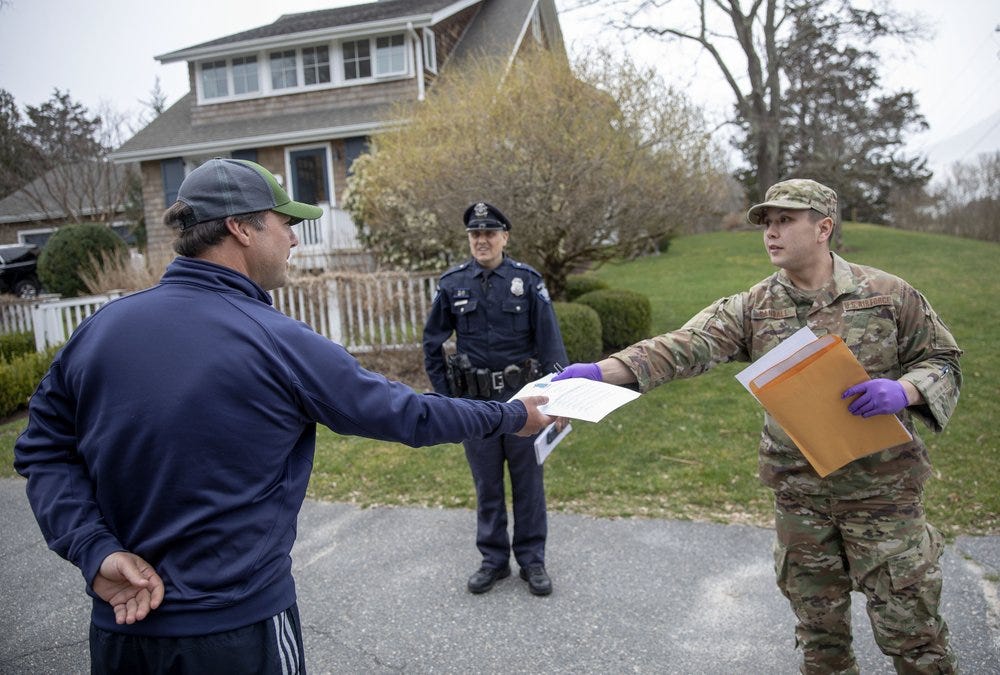 Rhode Island Air National Guard TSgt. William Randall, right, hands an information sheet to New York resident Reha Kocatas who is self-quarantining at his home in Westerly, R.I., Saturday, March 28, 2020. The Rhode Island National Guard started going door to door on Saturday in coastal areas to inform any New Yorkers who may have come to the state that they must self-quarantine for 14 days. (AP Photo/David Goldman)