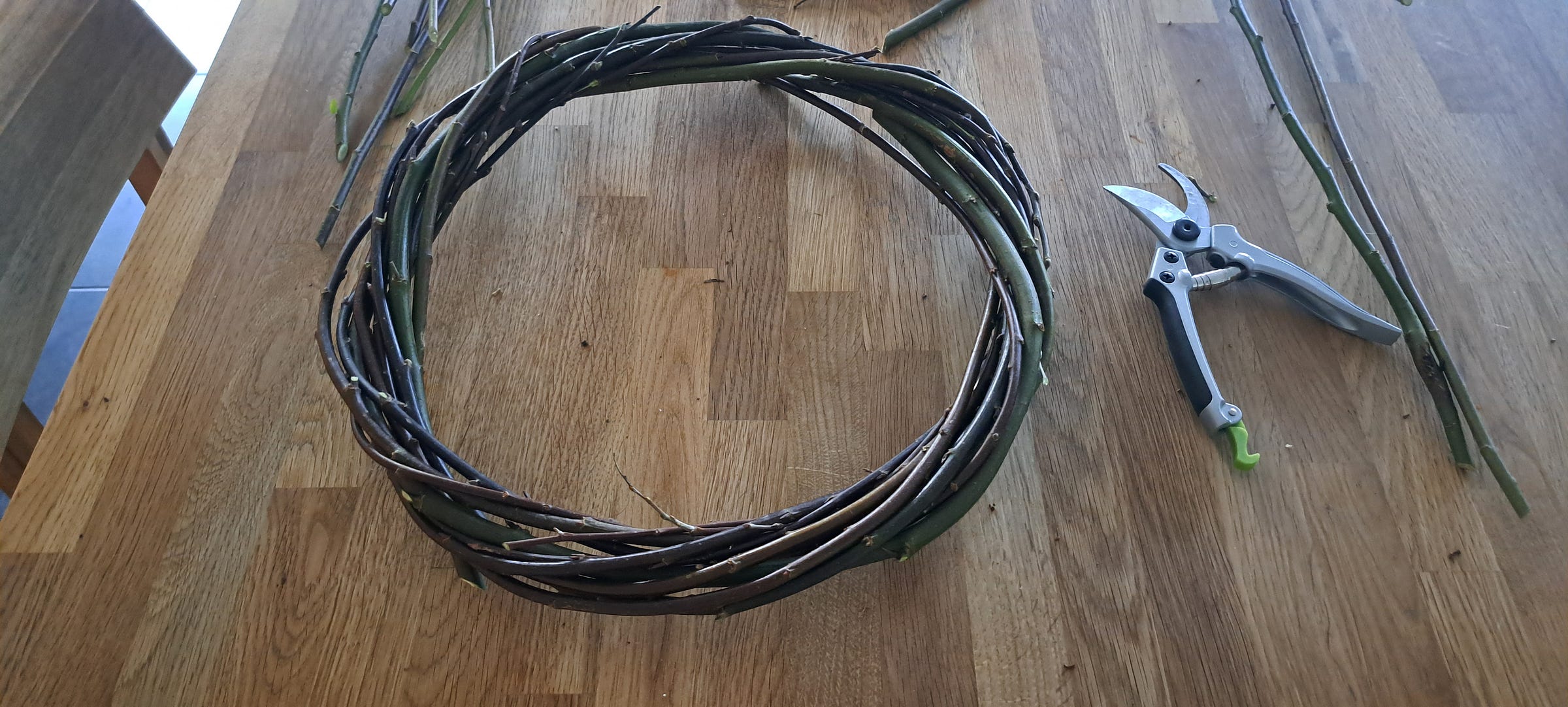 A round willow wreath base and secateurs on a wooden table.