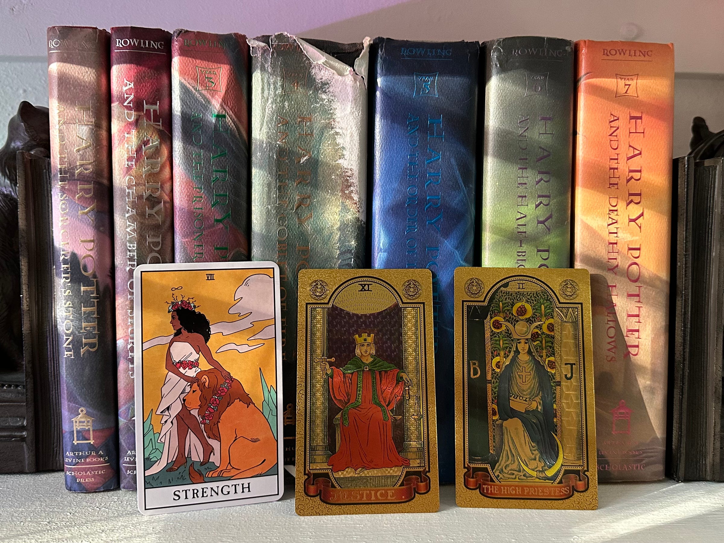 The Strength, Justice, and High Priestess Tarot cards rest against a collection of Harry Potter books on a bookshelf.