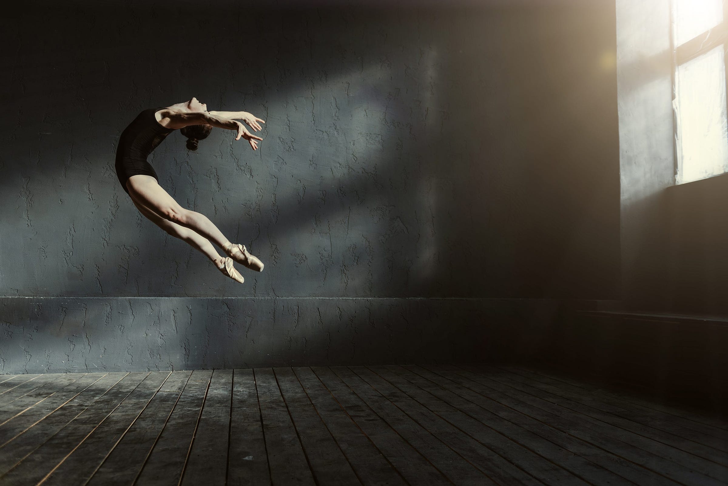 Professional ballet dancer performing in a grey, dark lighted room, window to the right