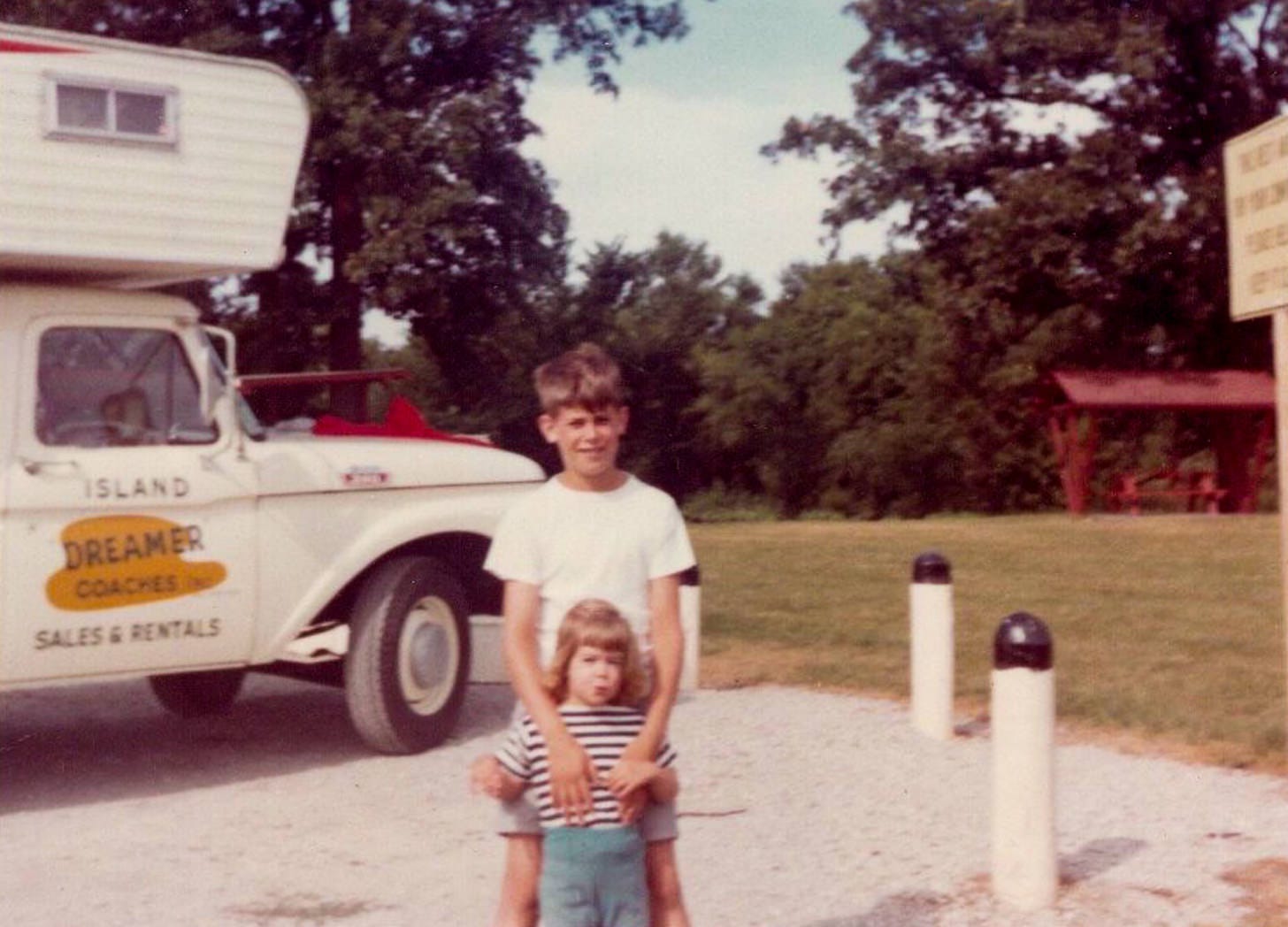 young boy with toddler girl standing in front of 1960's truck camper