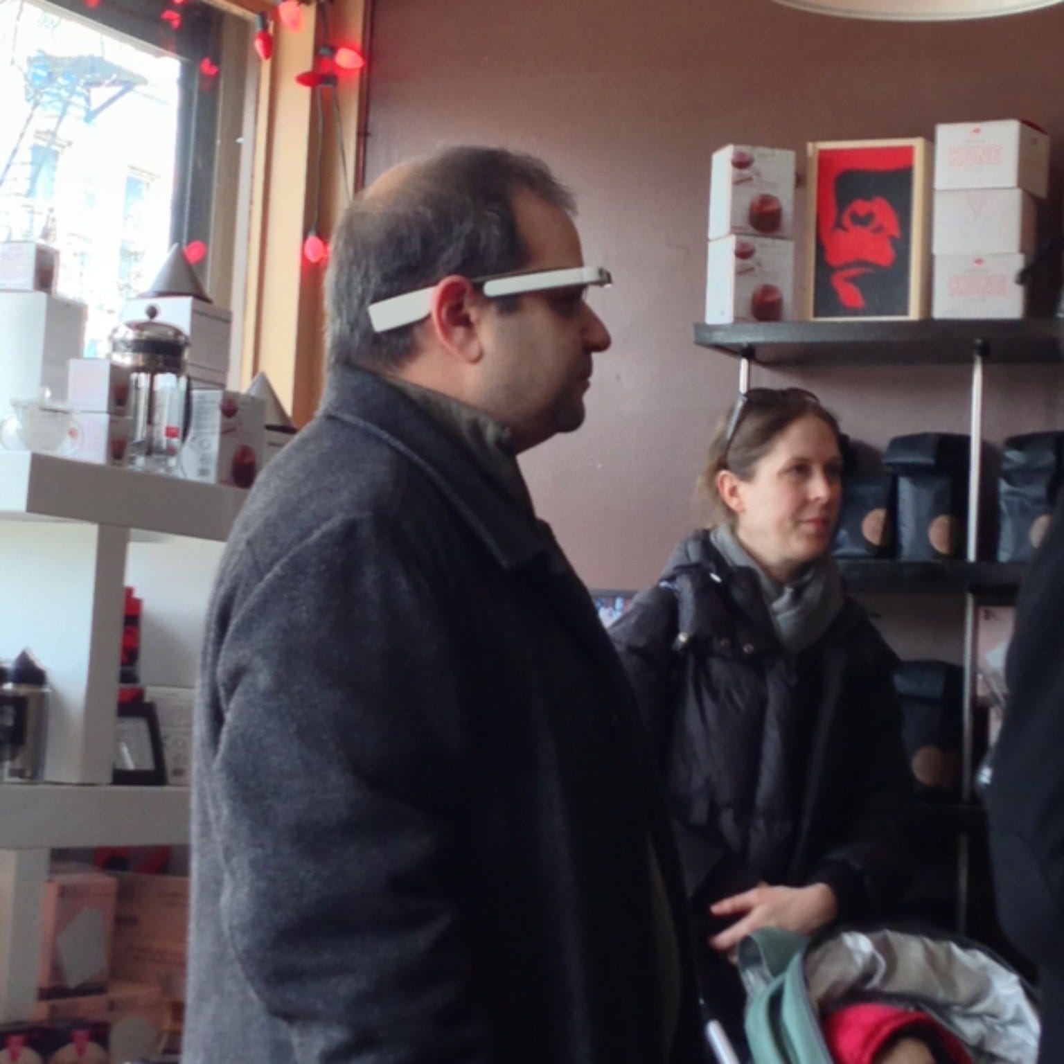 Photo of a man waiting in line at a coffee shop wearing Google Glass