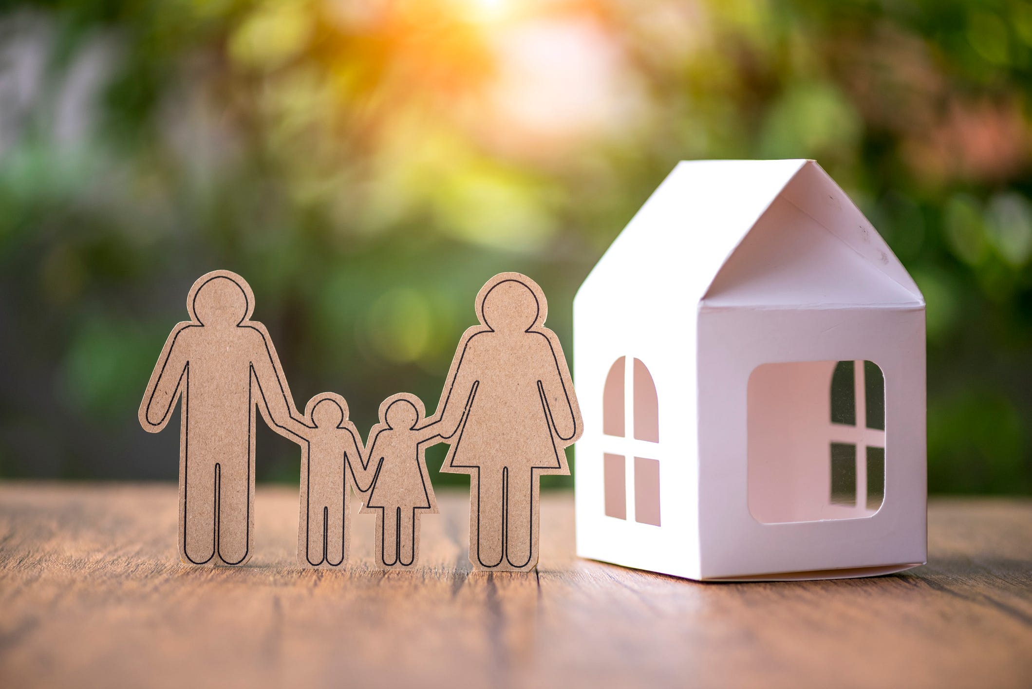 A paper family stands in front of a paper house.