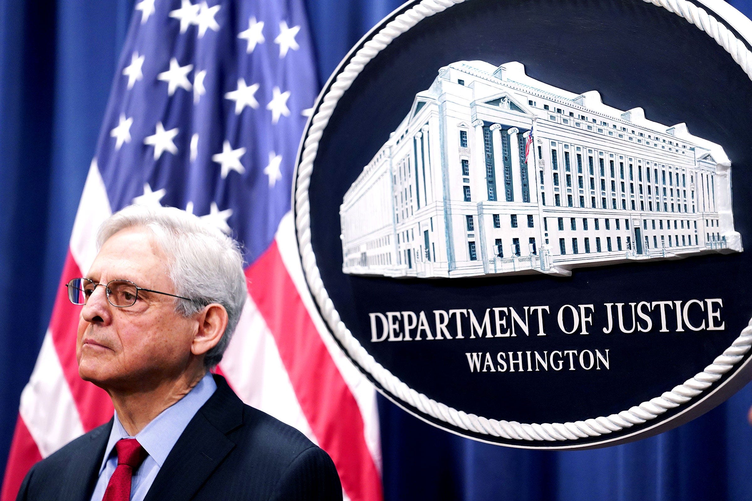 Merrick Garland standing in front of Department of Justice signage and an United States flag Merrick Garland standing in front of Department of Justice signage and an United States flag