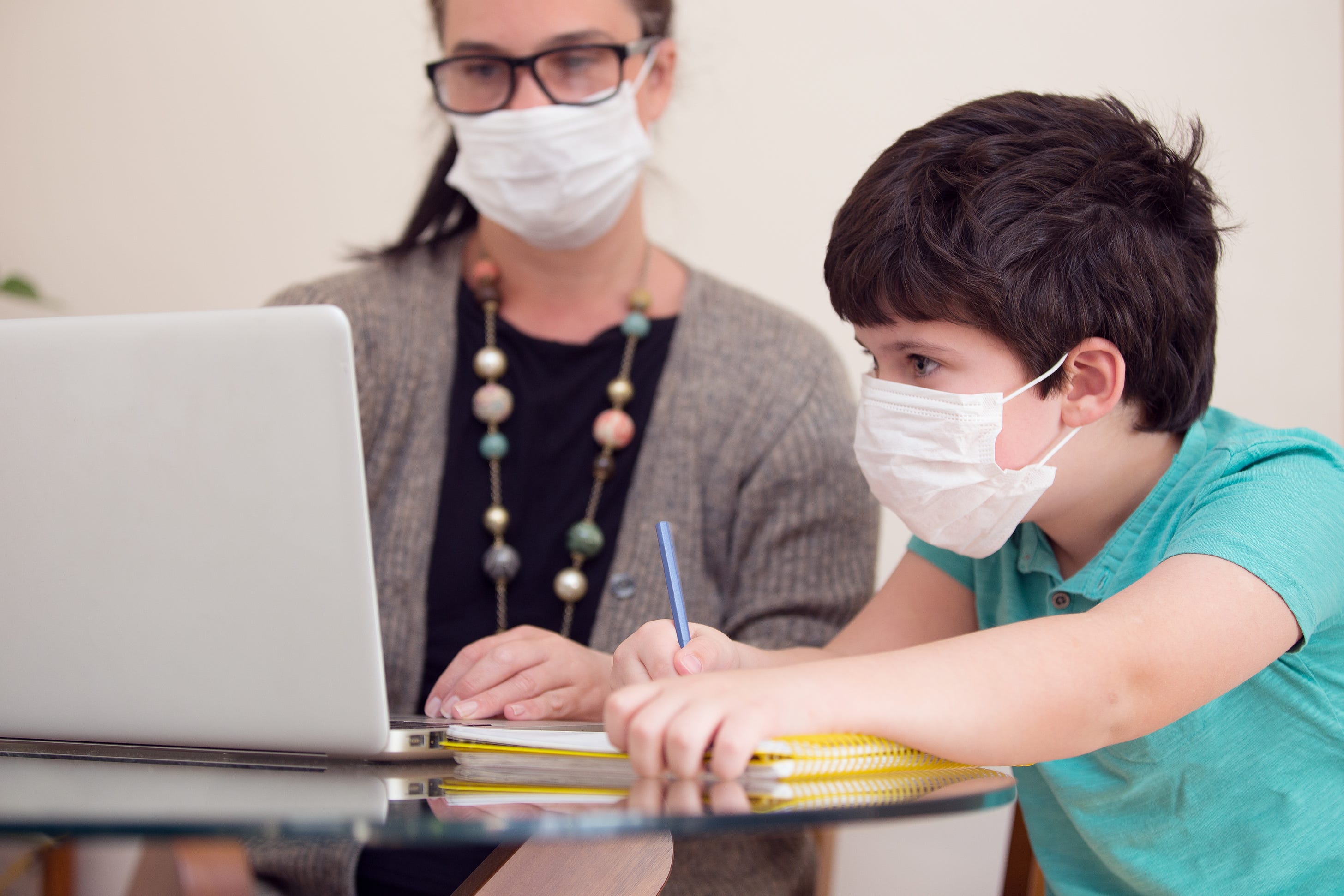 A student pores over a online lesson while a teacher looks on.