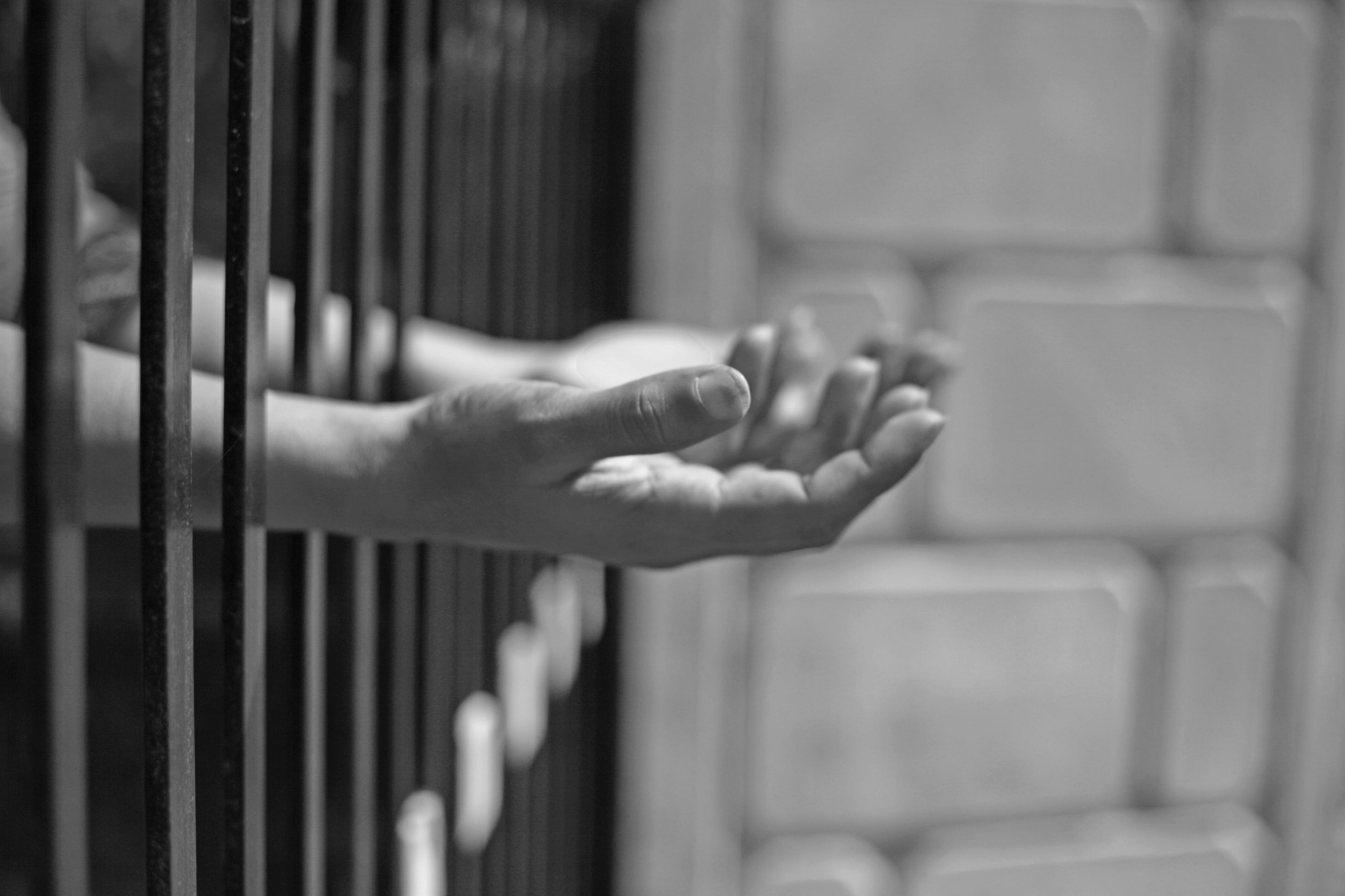 Upturned hands poke out of a prison cell.