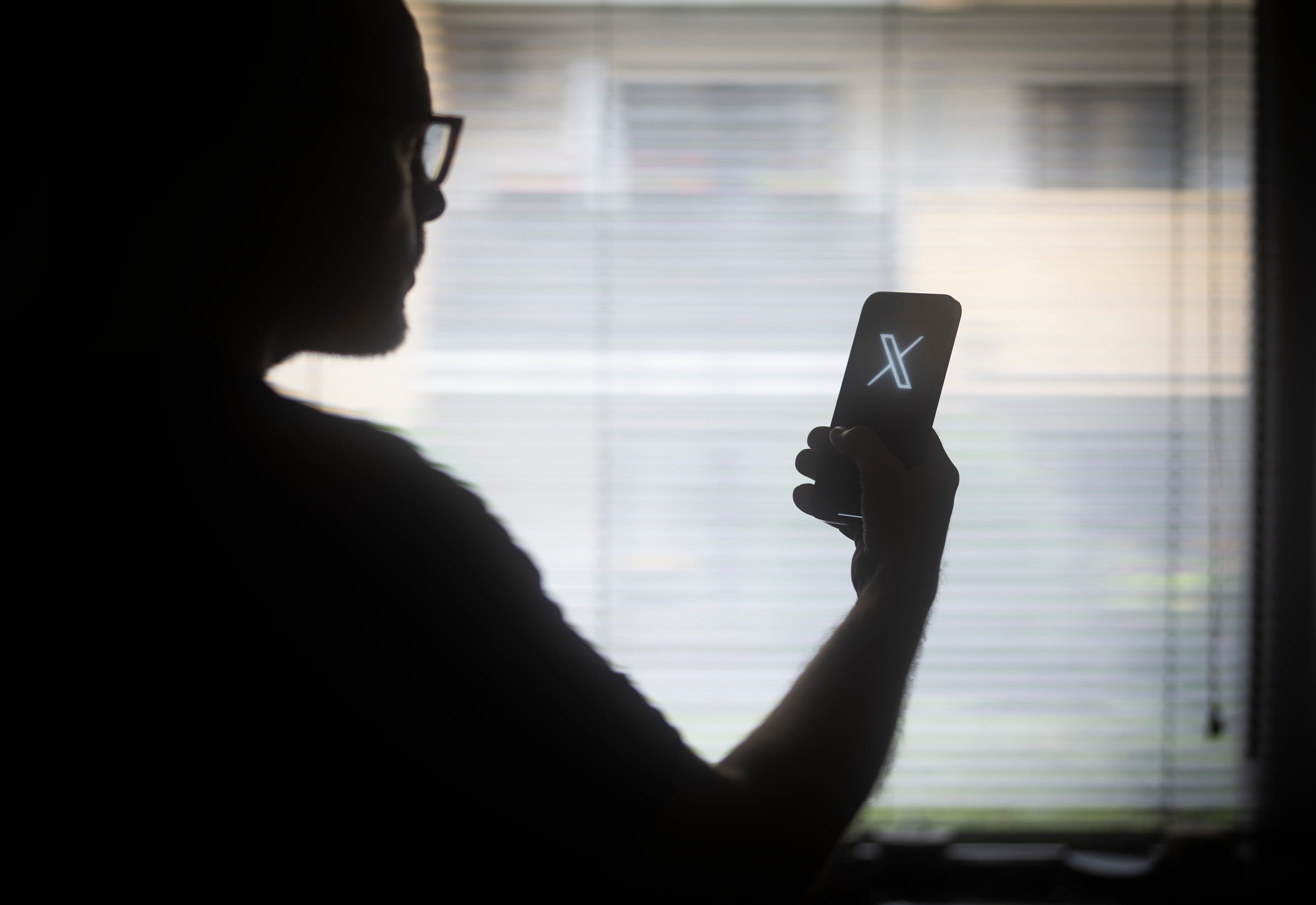 The X logo is seen on a mobile device held in the hand of a man with glasses in this illustration photo in Warsaw, Poland on 29 August, 2023. (Photo by Jaap Arriens/NurPhoto via Getty Images)