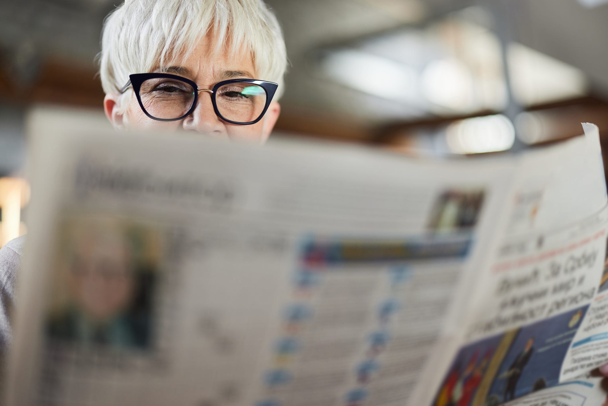 A woman intently reads a newspaper.