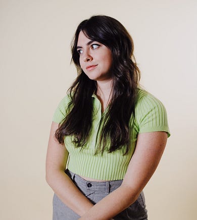 Portrait of Sam Speedy, Director of Digital Media for Padma Lakshmi and Delicious Entertainment. Wearing a green shirt against a beige background.
