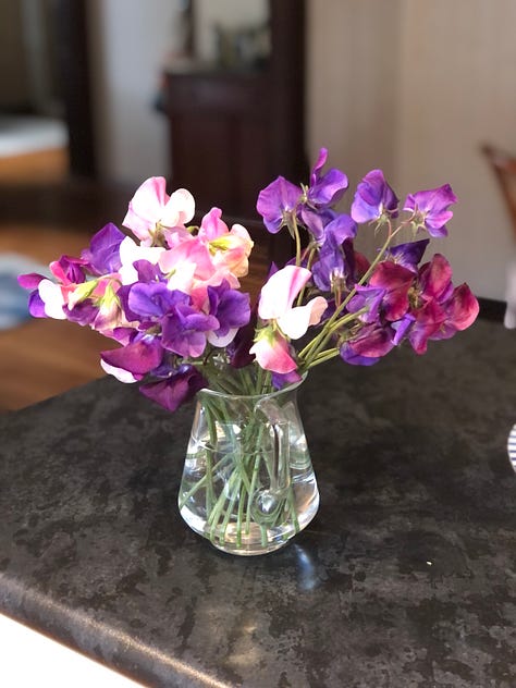 A vase of sweet peas, fresh vegetables and a stack of books