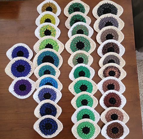 Rainbow knit flower earrings, a grey and green knit shawl, and rainbow knit eye patches.