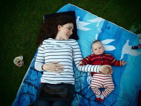 Woman with pram in a park beside a pond and a cat beside a black and white print of a happy couple. A woman on a picnic blanket with a baby in a garden