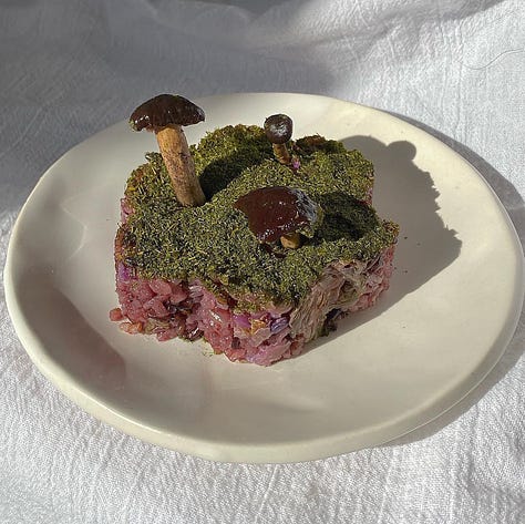 Butter intricately structured as a icing-piped cake with a single lit candle, oyster shells, and a mound of rice that looks as though it is mossy dirt with mushrooms from the forest