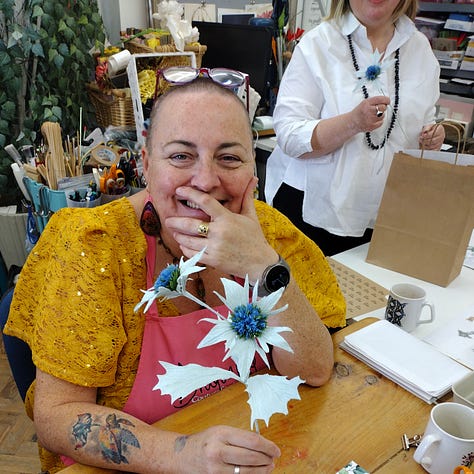 Image one depicts sea holly made from paper dyed with a ranof natural colours, 8mage 2 shows the natural plant growing in its natural beach environment, spiky, holly shaped leaves of a glowing, pale blue-green hue. Picture 3 shows students in the art studio holding their paper sea holly and smiling