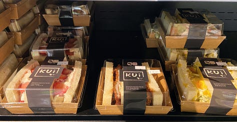 Left: piece of green pandan cake in clear plastic box; Center: Japanese-style packaged sandwiches; Right: Lays' Roasted Garlic Oyster flavor potato chips
