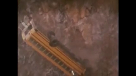 The bus plummets over the ledge and shatters like a toy below.