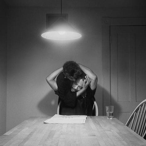1-9) All images are black and white, and involve a table, as well as a few chairs, and an overhead light. 1) A black woman is seen playing cards by herself. 2) A black woman is seen holding her head in her hands, while reading a book. There is a child sitting to her right, writing. 3) A black person is standing at the end of the table, looking into the camera. 4) A black woman is looking at herself in a tabletop mirror, while a child is playing to the right of her at the table. 5) Three people are sitting at the table, and appear to be playing a game or laughing. 6) A black woman is seen looking at herself in a tabletop mirror. 7) A black woman is sitting on the left side of the table, with her hand under her chin. There is a black man at the end of the table, reading the newspaper, with his hand resting on his neck. 8) Two black people are seen kissing/embracing. One is sitting at the end of the table, and the other person is behind them. 9) A black woman is seen with her head laying back on the table, with her hands in her hair.