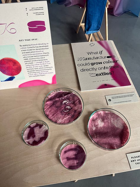 1-2. Exhibition table for 'pinks' from Ruth Lloyd and Colorifix showing fabric samples in petri dishes dyed directly with bacteria, and a vial of bacterial culture; 3. Pink bacteria-dyed fabrics hung up in the exhibition space with other brightly-coloured fabrics in the background.