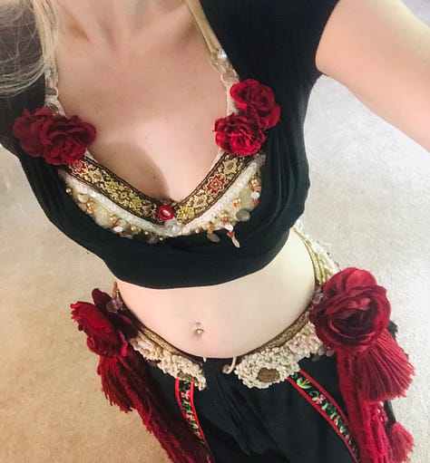 Costume trials in black pants and crop top, with cream and gold belt and bra covered in red tassels and roses. The last photo is one of the roses held in the palm with the red yarn dangles twined around the wrist.