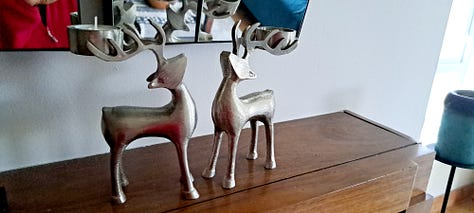 Six photos of stag decorations. 1. cushion with stag head; 2.  2 small black wooden deer ornaments; picture in frame of stag against blue background with message 'Season's Greetings'; white wooden stag figure; two silver stags facing each other with their antlers as candleabra; delicate white ceramic stag tree decoration.