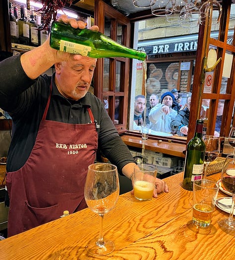 A Bar Nestor employee pouring cider into a glass, overhead shot of a tomato salad, over head shot of a cooked, sliced steak