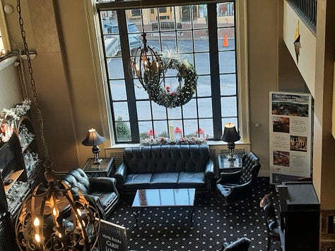 A collage of photos showing the Historic Hotel Bethlehem, including two photos of the 9-story brick exterior, and interior pictures of the elevators, white marble staircase with polished handrail, open doors to the ballroom with a glistening chandelier, and two photos of the lobby, with luxurious black leather furniture in front of a huge arched window with a Christmas wreath in the middle. Also a look inside a room of a bed with a robe lying on the end.