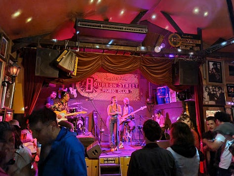 Photo 1: Image of a painting showing a mother and baby, the baby has a 6 pack. Photo 2: Aisling on a large bronze rocking horse. Photo 3: Photo of a band on a stage with a sign reading Bourbon Street Music Club.