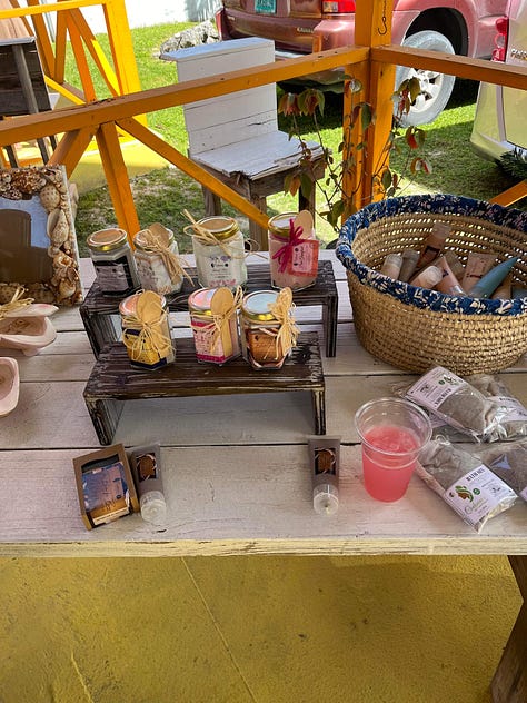 Left to right: Wodden tables with jars of homade body scrubs and lotions. Wodden Tables with homemade soaps. Table with a red table cloth featuring Bahama sponges