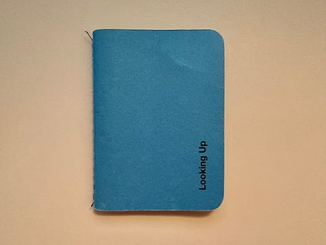 Photographs of a small blue book called "Looking Up", including one photo of the front cover, another photo of the introduction message on the book's first page, and another photo of a page reflecting on the purpose of ad agencies being to buy more stuff.