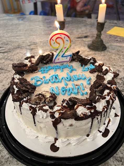 toddler holding blue nyon 2 balloon, 2nd birthday cake, a snippet from FURY, snow falling near a street lamp, kids looking at snow through the window, snow