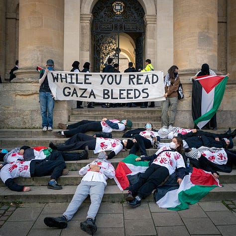 people wearing white t-shirts with red handprints on them lie on the steps outside the Sheldonian building in Oxford as others queue up in academic gowns. photos courtesy of @madeleine_observes