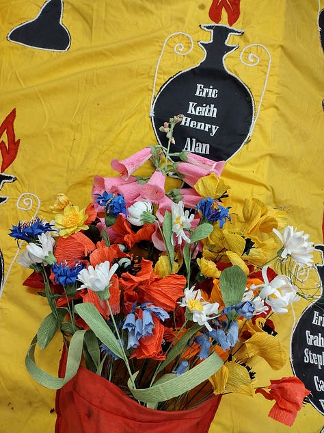 Brightly coloured paper poppies and paper wildflowers arranged in the red and yellow Hillsborough Memorial Banner