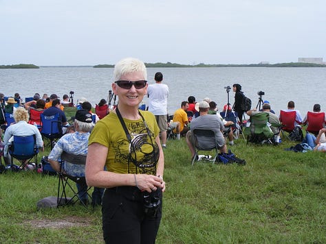 Three photos. First photo: a woman with short cropped blond hair, with green t-shirt, black pants. With binoculars. In the background, a body of water. In the far background, the Space Shuttle on the launchpad. Second and Third photos: images of the Space Shuttle Atlantis STS 135 on the launch pad.