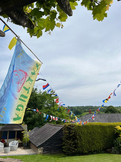 A blue and yellow flag with the boat's name "Tartuga" on it, with imagers of a fish and a pen (our dual passions) billowing against blue sky